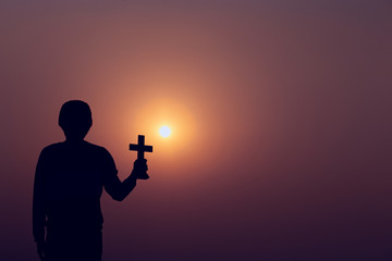 Wall Mural - Human holding christian the Cross with light sunset background, Christians should worship and thank God, Christian silhouette concept.