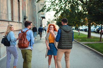 Group of smiling tourists enjoying on vacation, young friends having fun walking on city street during the day.