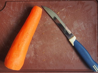 On a plastic cutting Board is a boiled carrot and a knife.