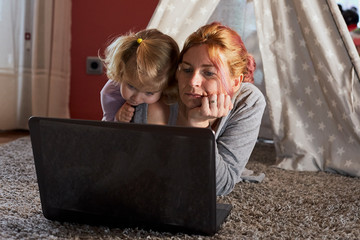 caucasian woman with little girl consulting laptop at home