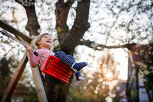 Happy Beautiful Little Toddler Girl Having Fun On Swing In Domestic Garden. Cute Healthy Child Swinging Under Blooming Trees On Sunny Spring Day. Baby Laughing And Crying