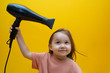 © Afina - Cute smiling little girl dries hair on the yellow background.