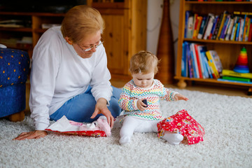 Wall Mural - Cute little toddler girl and grandmother playing with toys at home. Adorable baby child and senior retired woman unpacking gifts for birthday. Happy family together