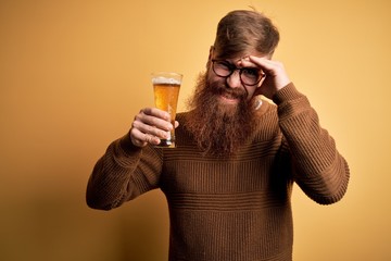 Sticker - Irish redhead man with beard drinking a glass of refreshing beer over yellow background stressed with hand on head, shocked with shame and surprise face, angry and frustrated. Fear and upset