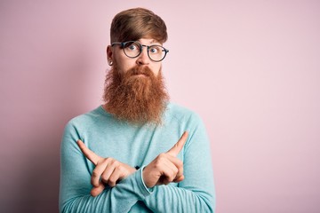 Poster - Handsome Irish redhead man with beard wearing glasses over pink isolated background Pointing to both sides with fingers, different direction disagree