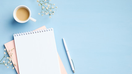 Fototapete - Flat lay, top view feminine workspace with blank notepad, cup of coffee, pen and flowers on blue background. Minimal style home office desk, business and education concept
