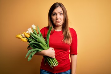 Canvas Print - Young blonde woman holding romantic bouquet of tulips flowers over yellow background depressed and worry for distress, crying angry and afraid. Sad expression.