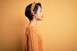 © Krakenimages.com - Young beautiful asian girl wearing casual sweater and diadem standing over yellow background looking to side, relax profile pose with natural face and confident smile.