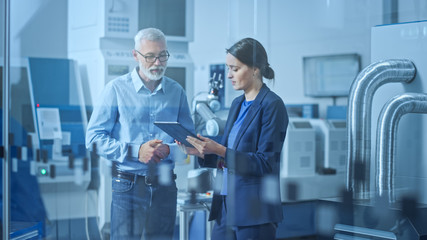 Fototapete - Modern Factory: Female Engineer, Male Project Manager Standing in High Tech Development Facility, Talking and Using Tablet Computer. Contemporary Facility with CNC Machinery, Robot Arm Production Line