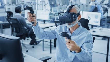 Leinwandbilder - Industrial Design Engineer Wearing Virtual Reality Headset and Holding Controllers, Uses VR technology for Industrial Design, Development using Computer. Modern Factory Office, Workshop with Machinery