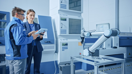 Poster - Modern Factory: Female Project Manager and Male Engineer Standing, Talking and Using Tablet Computer for Programming Robot Arm Assembly Line. Contemporary Facility with High Tech CNC Machinery