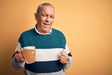 Sticker - Senior handsome man drinking jar of beer standing over isolated yellow background winking looking at the camera with sexy expression, cheerful and happy face.