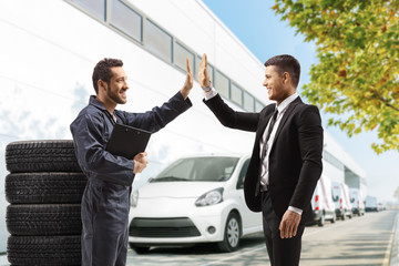  Auto mechanic gesturing high-five with a professional man outside a car service building