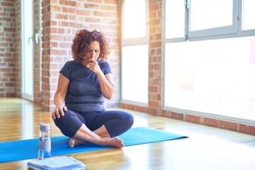 Middle age beautiful sportswoman wearing sportswear sitting on mat practicing yoga at home feeling unwell and coughing as symptom for cold or bronchitis. Healthcare concept.