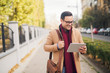 © Jelena - Businessman standing on the street and using tablet.