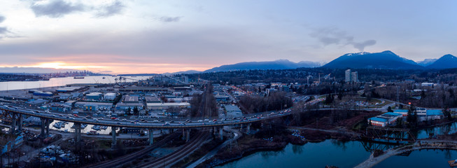 Aerial drone shot of commuter traffic on the Second Narrows bridge and the industrial port facilities in Vancouver, BC, Canada at sunset.