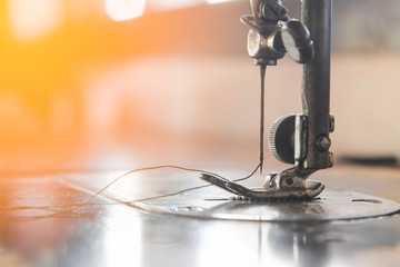 Needle presser foot with thread of vintage old sewing machine for sew cloth with bokeh and orange light close-up.