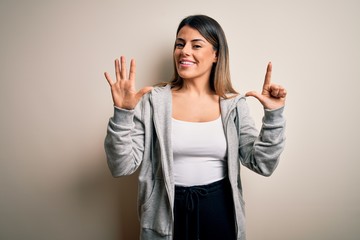 Wall Mural - Young beautiful brunette sportswoman wearing sportswoman training over white background showing and pointing up with fingers number seven while smiling confident and happy.