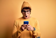 Young Handsome Man Using Smartphone Wearing Glasses Over Isolated Yellow Background Scared In Shock With A Surprise Face, Afraid And Excited With Fear Expression