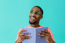 Portrait Of A Happy  Young Person Reading With Glasses Holding Book And Looking Up, Isolated On Blue Copy Space