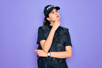 Sticker - Young police woman wearing security bulletproof vest uniform over purple background with hand on chin thinking about question, pensive expression. Smiling with thoughtful face. Doubt concept.