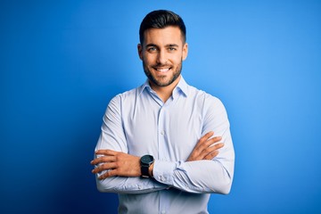 Wall Mural - Young handsome man wearing elegant shirt standing over isolated blue background happy face smiling with crossed arms looking at the camera. Positive person.