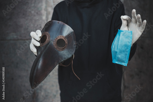 Man holds a mask of plague doctor and disposable medical mask. Epidemic protection. No face.