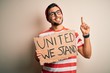 © Krakenimages.com - Handsome activist man protesting wearing glasses holding cardboard with unity message surprised with an idea or question pointing finger with happy face, number one