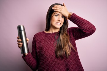 Canvas Print - Young beautiful girl holding thermo with water standing over isolated pink background stressed with hand on head, shocked with shame and surprise face, angry and frustrated. Fear and upset