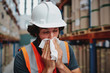 © StratfordProductions - Young warehouse worker feeling sick while sneezing and coughing at factory standing near packed cardboard boxes on shelf