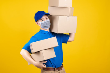 Delivery handsome man wearing mask with heavy many carton box picking up the package to front home receiver shipping deliver cargo prevention infected virus on yellow background isolated studio shot.