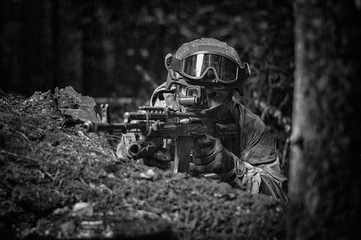 Portrait of a soldier in the forest. He sits in cover and prepares to shoot. Border Protection Concept.