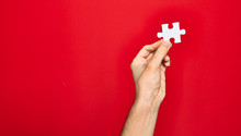 Beautiful Hand Of Man Holding Piece Of Puzzle Over Isolated Red Background