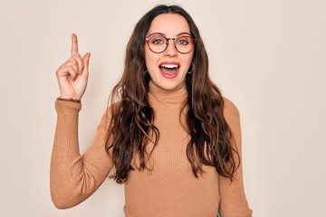 Wall Mural - Young beautiful woman wearing casual turtleneck sweater and glasses over white background pointing finger up with successful idea. Exited and happy. Number one.