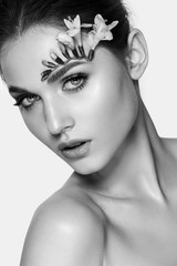 Wall Mural - Beautiful, young, natural, girl with natural make-up and a living flower over an eyebrow, posing in the studio on a white background. Black and white photography.