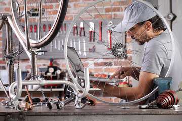 man repair the vintage bicycle at the computer search spare parts and see internet in garage workshop on the workbench with tools, diy concept