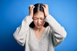 Young beautiful asian woman wearing casual sweater standing over blue isolated background suffering from headache desperate and stressed because pain and migraine. Hands on head.
