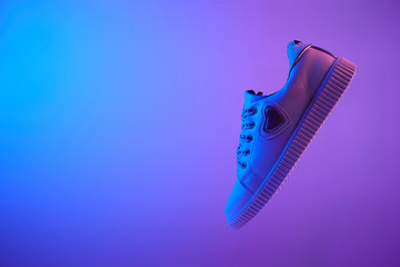 Wall Mural - Trendy white teenage sneaker flying in trendy neon light. Levitation Shoe in red, blue light. Creative minimalism.