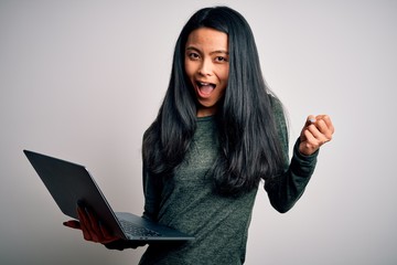 Wall Mural - Young beautiful chinese woman using laptop standing over isolated white background screaming proud and celebrating victory and success very excited, cheering emotion