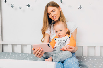 a happy mother and a small child relax while lying on the bed, holding a mobile phone and looking at