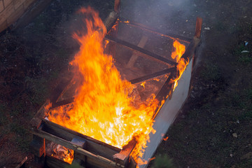 Fire coils over a burnt building. A pile of coals at the site of a burnt shed. Bright flames, flying ashes of a burning wooden building during a fire