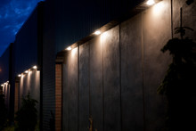 Large Pot Lights Illuminating A Concrete Wall With Bricks At Twilight. Illuminated Blank Building Wall In The Dark.