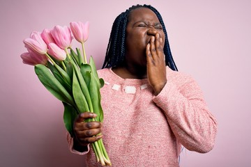 Sticker - Young african american plus size woman with braids holding bouquet of pink tulips flower bored yawning tired covering mouth with hand. Restless and sleepiness.