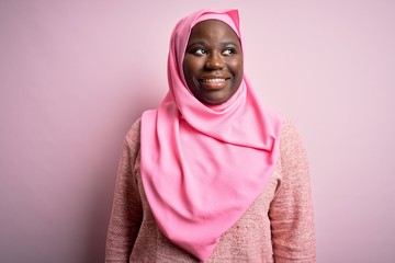 Canvas Print - Young african american plus size woman wearing muslim hijab over isolated pink background looking away to side with smile on face, natural expression. Laughing confident.