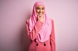 © Krakenimages.com - Young beautiful brunette businesswoman wearing pink muslim hijab and business jacket looking confident at the camera smiling with crossed arms and hand raised on chin. Thinking positive.