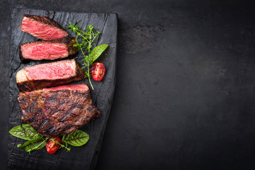 Wall Mural - Barbecue dry aged wagyu entrecote beef steak with lettuce and tomatoes as top view on an old charred wooden board with copy space right