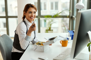 Wall Mural - Smiling businesswoman eating while using desktop PC in the office.