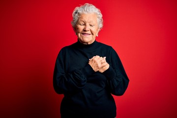 Wall Mural - Senior beautiful woman wearing casual sweater standing over isolated red background smiling with hands on chest with closed eyes and grateful gesture on face. Health concept.