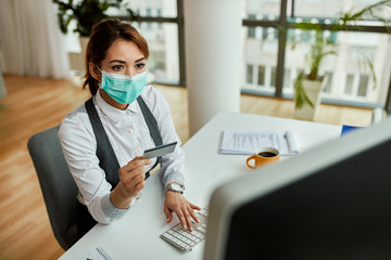 Wall Mural - Businesswoman with face mask using computer and credit card for online shopping in the office.