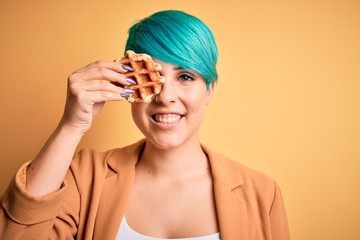 Sticker - Young woman with blue fashion hair holding delicious wffle over yellow background with a happy face standing and smiling with a confident smile showing teeth